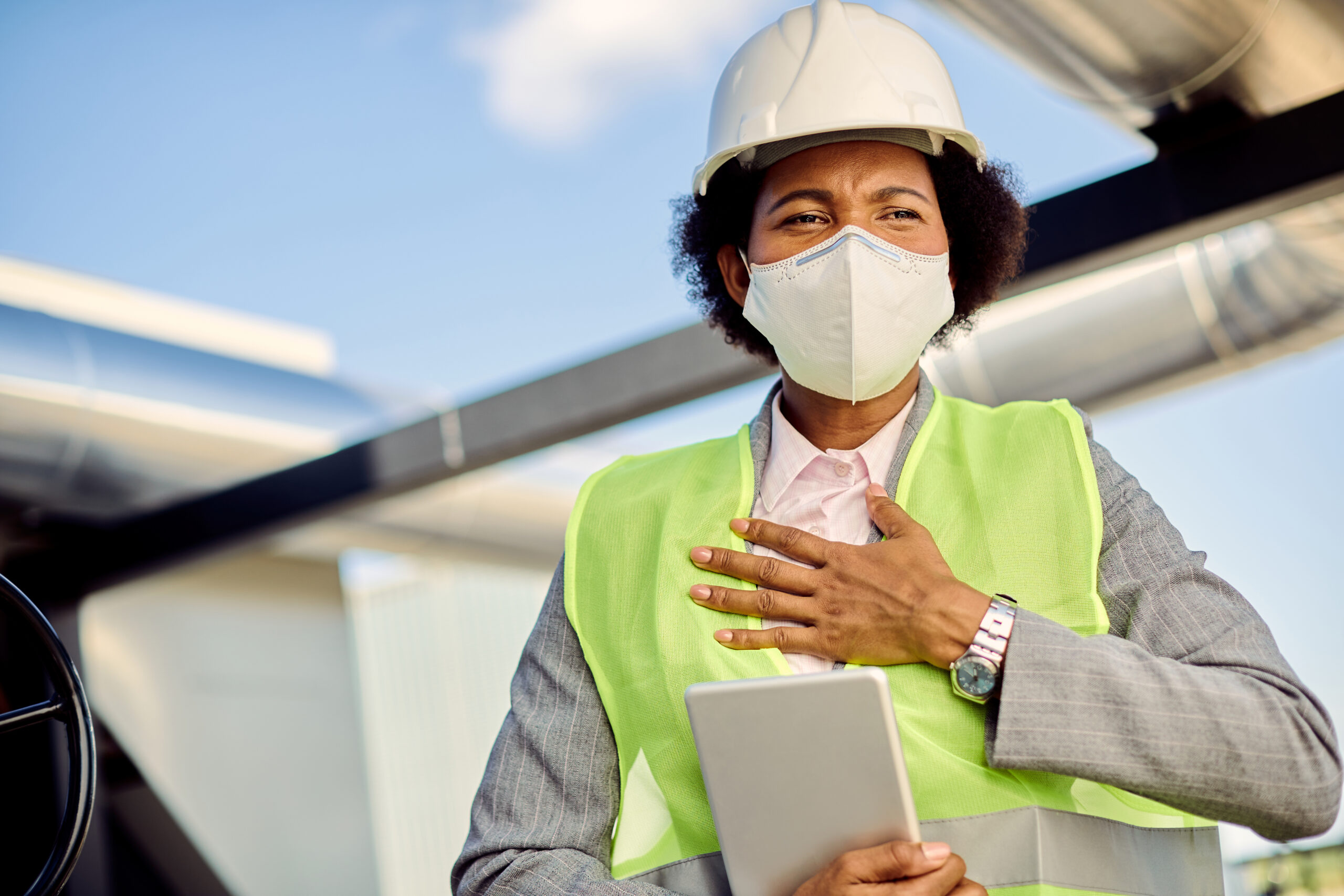 African American civil engineer holding her chest in pain while wearing protective face mask and working during COVID-19 epidemic.